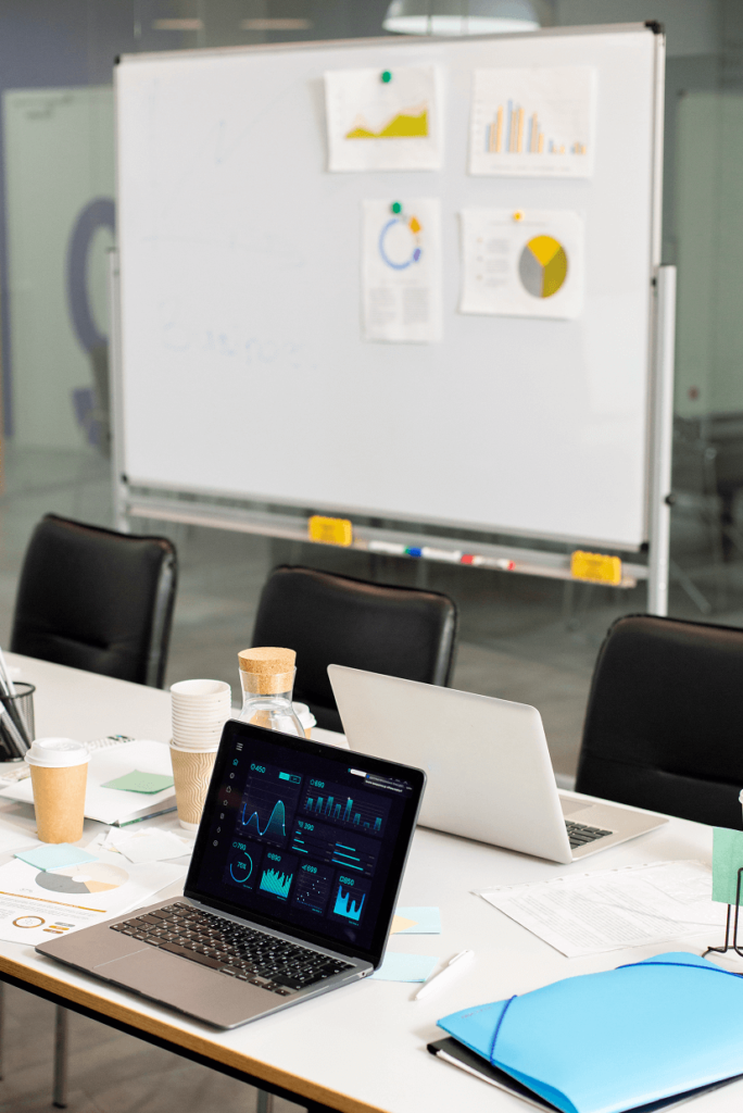 ReplaceMyselfAI business strategy meeting workspace with laptop analytics dashboard and whiteboard charts.